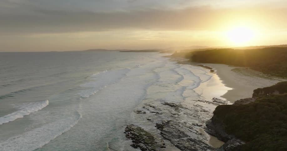 Waves flow onto the beach bordering the forest as the sun sits on the horizon