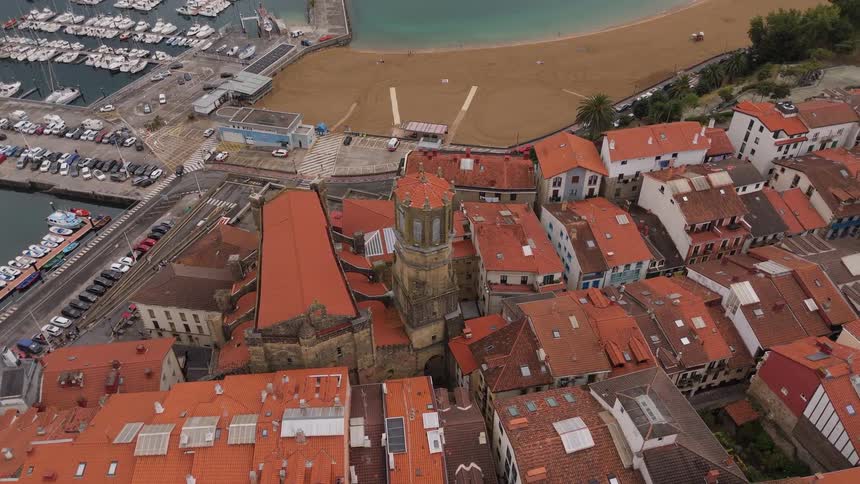 An aerial view of a residential neighborhood near the coastline shows buildings with red roofs at midday
