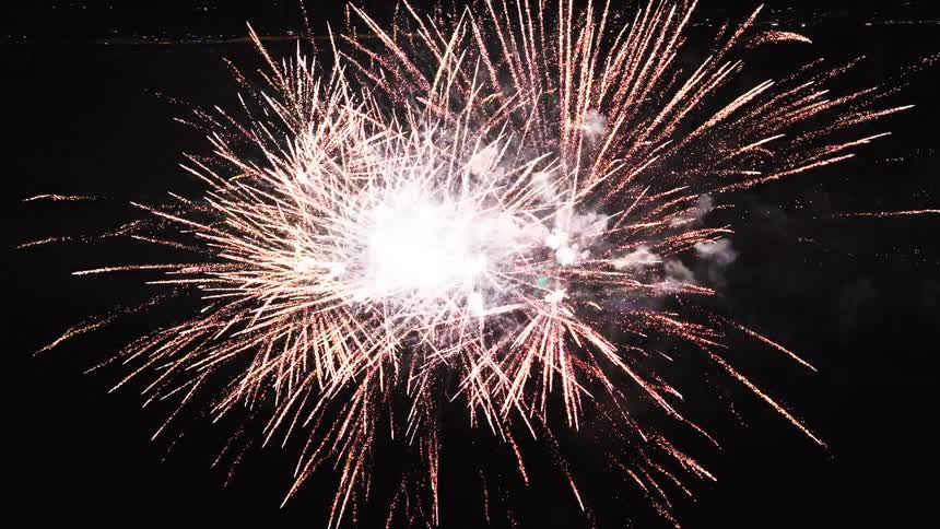 Burst of golden and white fireworks spreads across night sky with glowing trails