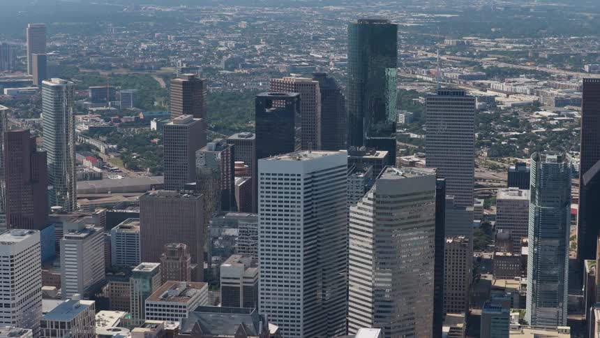 A slow aerial shot drifts over a dense downtown core revealing a sprawling city with countless skyscrapers gleaming under a bright hazy sky