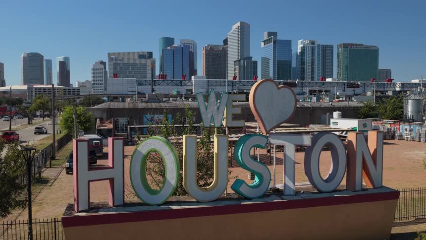 Houston sign outside of the city with towers and skyscrapers in the distance and traffic on the highway