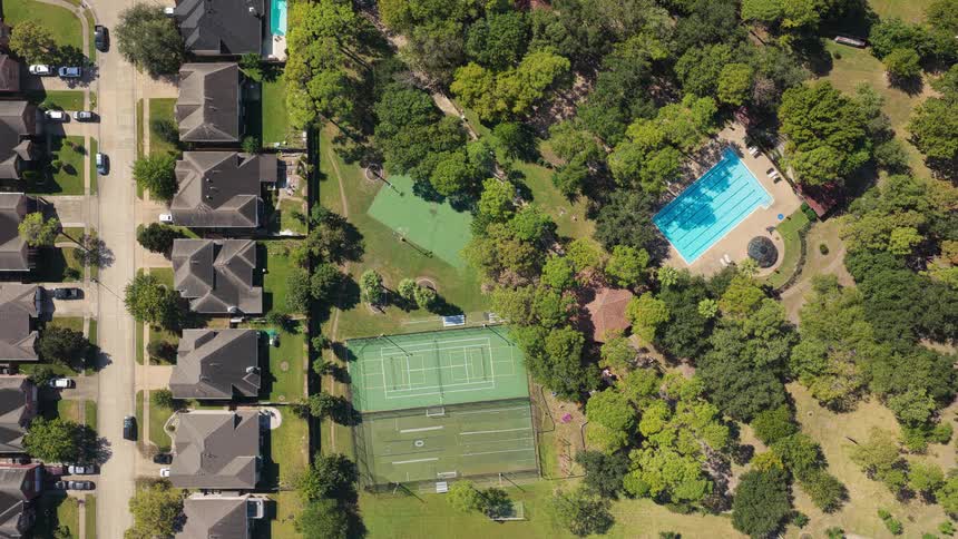 Park located next to a residential neighborhood contains sports fields and a swimming pool as well as many trees