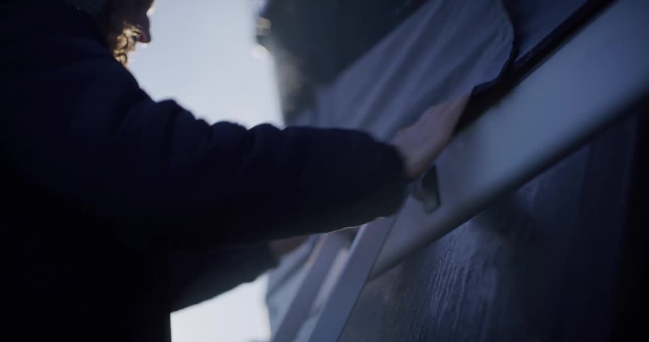 A man wearing a coat with a hood is zipping up a tent