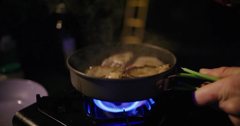 Meat is fried over blue flame with steam rising from the pan