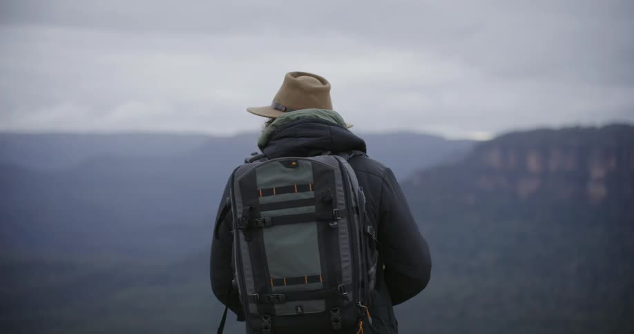 A man wearing a hat and backpack turns to look out over a misty mountain valley