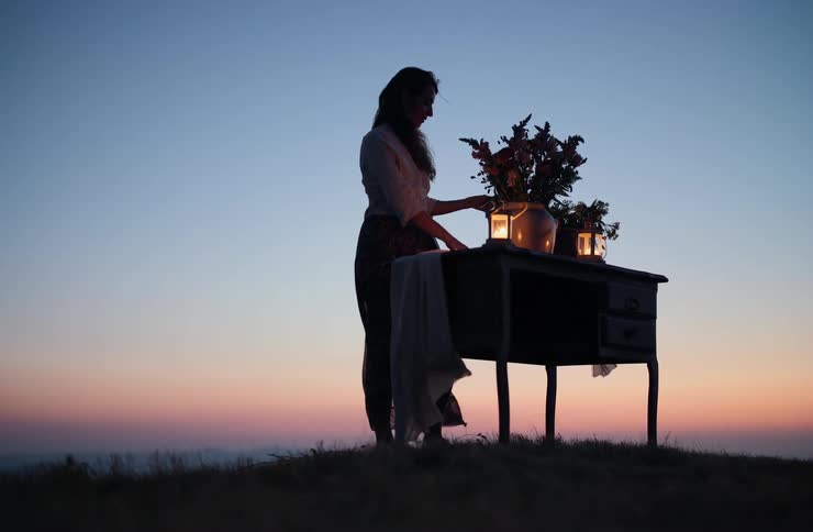 Silhouette of a woman beside a table with flowers and lanterns during sunset