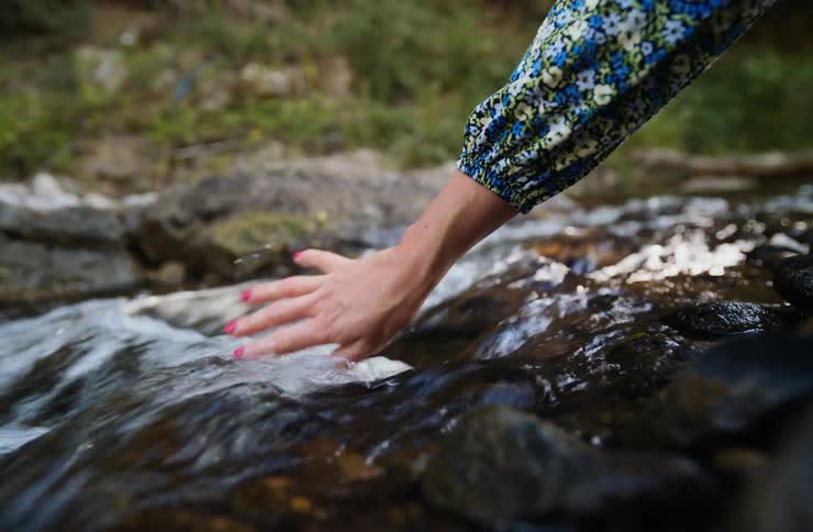 Hand touching the flowing water of a creek between rocks