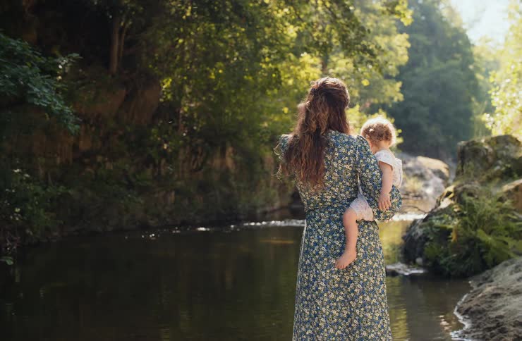 A mother carrying a baby near a river
