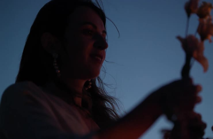 Woman holding flowers in a closeup with low lighting and a dark blue sky in the background