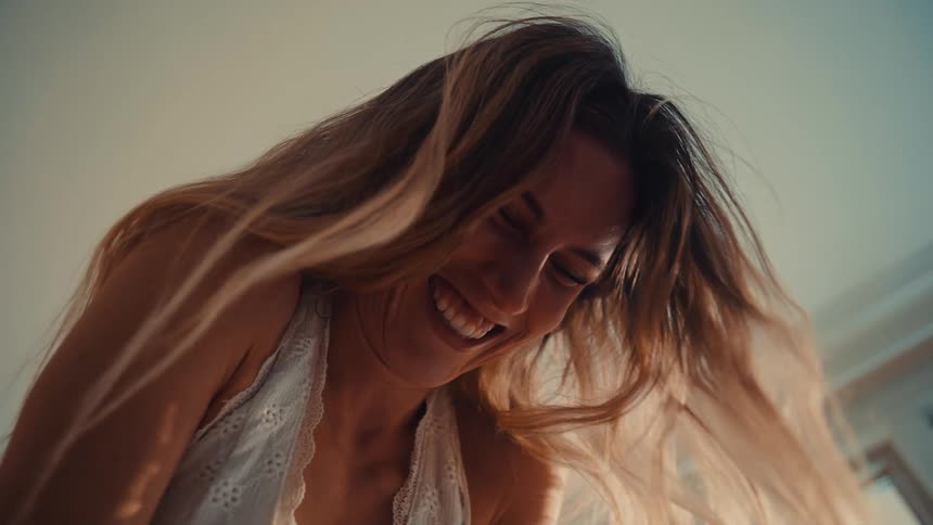 A young woman indoors laughs joyfully her long blonde hair scattered as she has fun