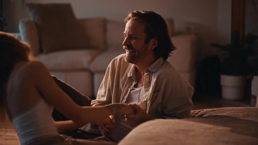 Couple sitting on the floor sharing smiles and holding hands in a cozy living room