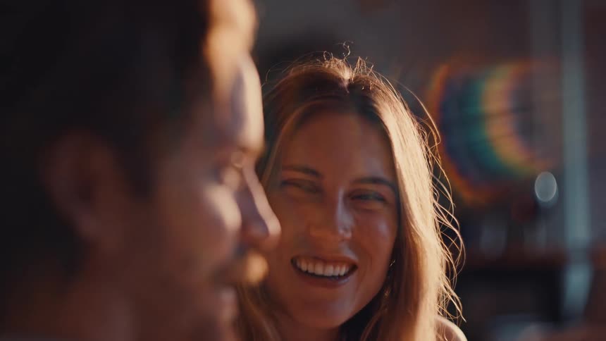A woman laughs affectionately near a man in warm golden light