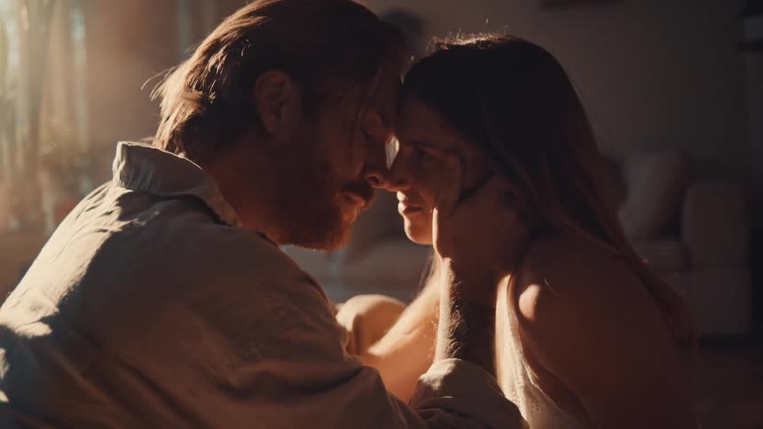 Couple sitting with foreheads touching while facing each other under soft indoor light