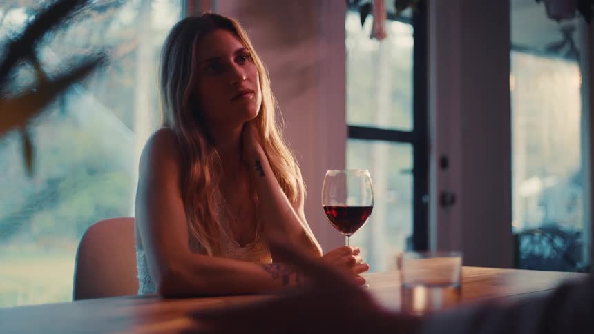 Woman sitting at the table holding a glass of wine while looking at the person in front of her
