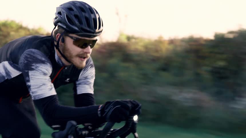 Man wearing sunglasses and a helmet rides fast on his bicycle