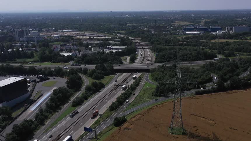 A sixlane highway three lanes in each direction runs horizontally across the lower middle of the frame with trucks and cars driving on itan overpass part of another road or highway crosses perpendicularly over the sixlane highway in the center o