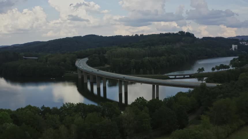 Traffic crosses the water between forested areas as mist covers the town in the background
