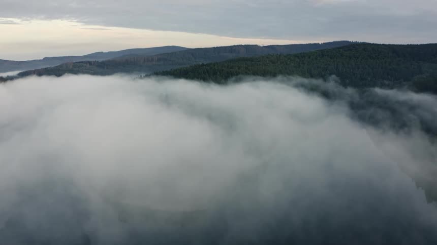 Dense fog obscures the water and the nearby forested mountains on a cloudy day