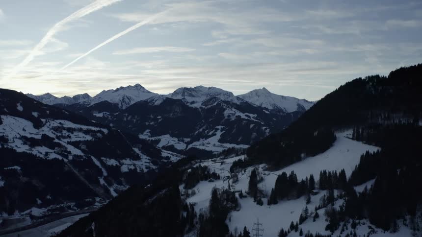 An epic aerial view drifts through a vast snowcovered mountain valley at dawn revealing majestic shadowy peaks against a cool sky