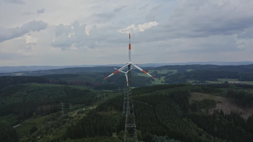 Aerial view of turbines spinning on a wind farm at the edge of a mountain