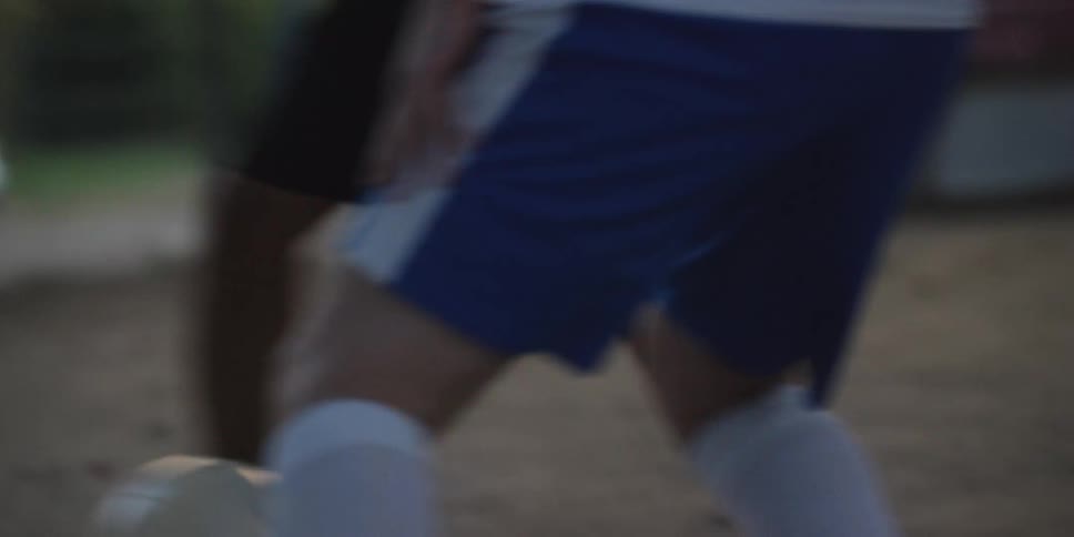 With intense rapid footwork a soccer player dribbles a ball across a dusty field skillfully maneuvering past a lunging defender in a closeup chase