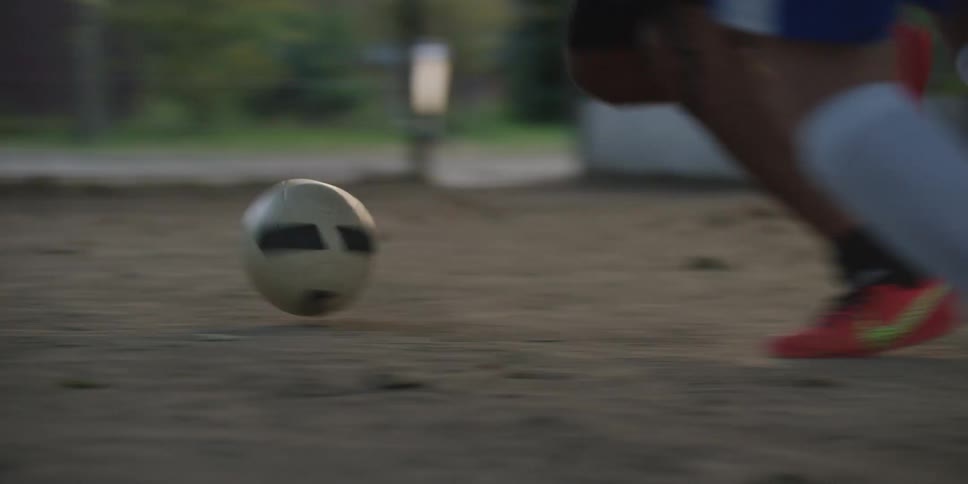 A lowangle shot follows two soccer players feet as they fiercely compete to dribble the ball across a dusty dirt pitch