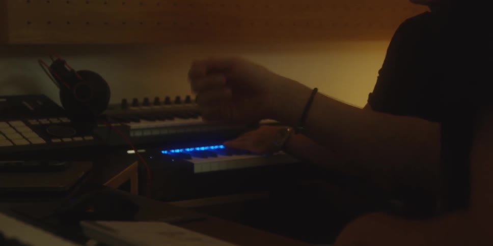 Hands operating music production equipment at a lit workstation