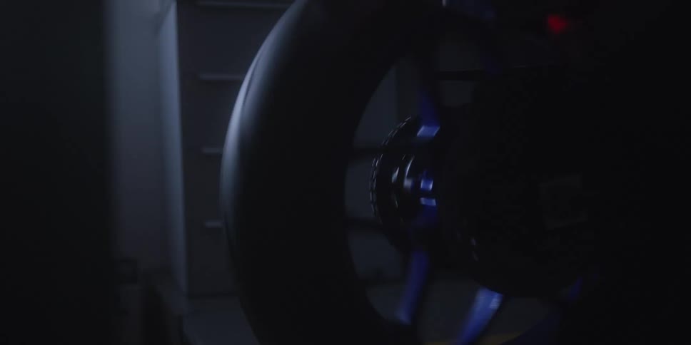 Spoked wheel stands out under bluish lighting in dark setting with furniture in background
