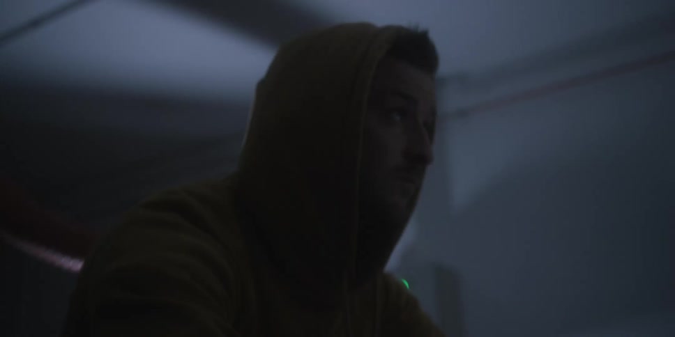 Hooded man in a dark environment looking forward under soft light