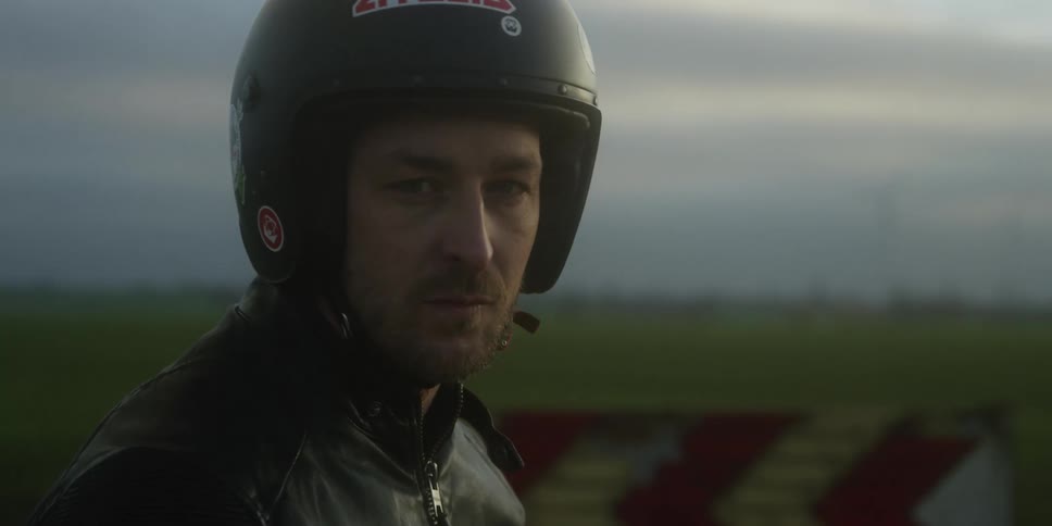 A motorcycle rider wears a black helmet and black leather jacket outdoors