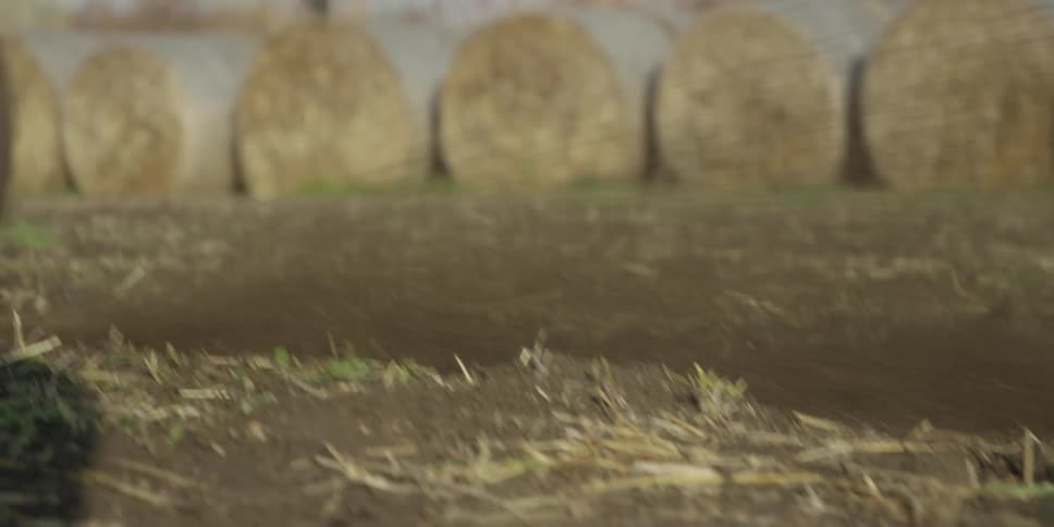 The rear wheel of a dirt bike spins rapidly kicking up dirt and debris from a dry muddy trackthe closeup shot quickly pans down as the bike speeds forward revealing hay bales in the blurry background