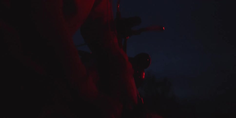 Hooded figure leaning forward under red lighting in the dark