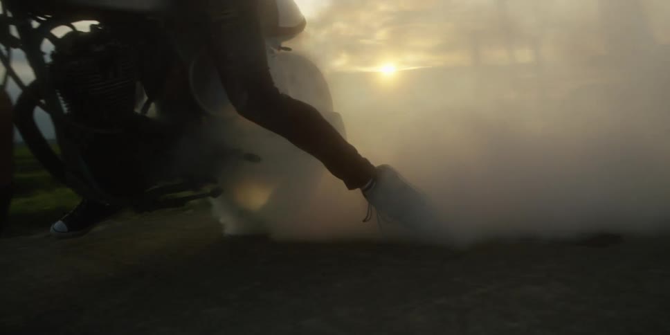 Cyclist rides their motorcycle on a rural road leaving a trail of smoke from the exhaust