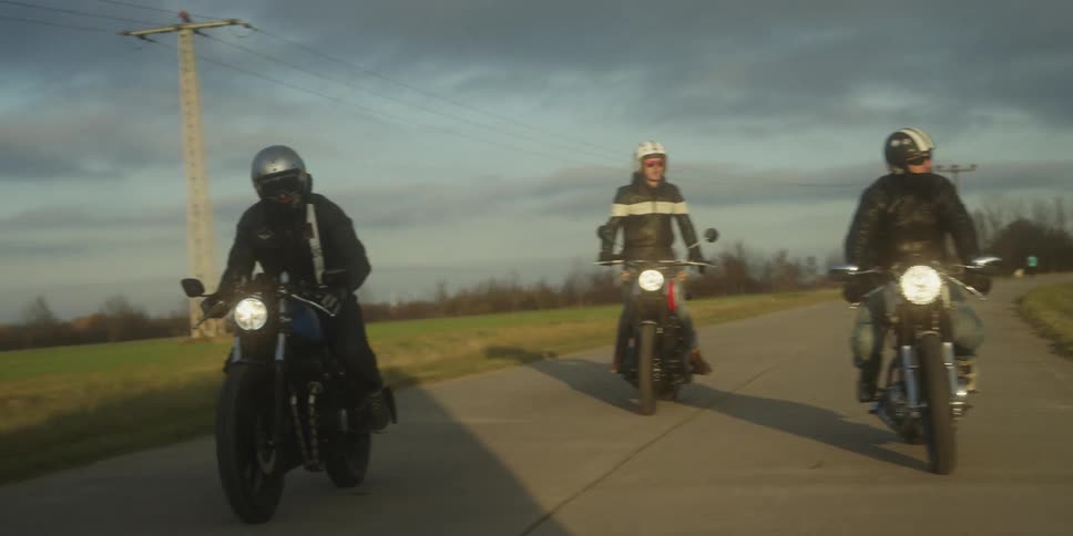 Four motorcyclists ride together down an open country road under a bright sky