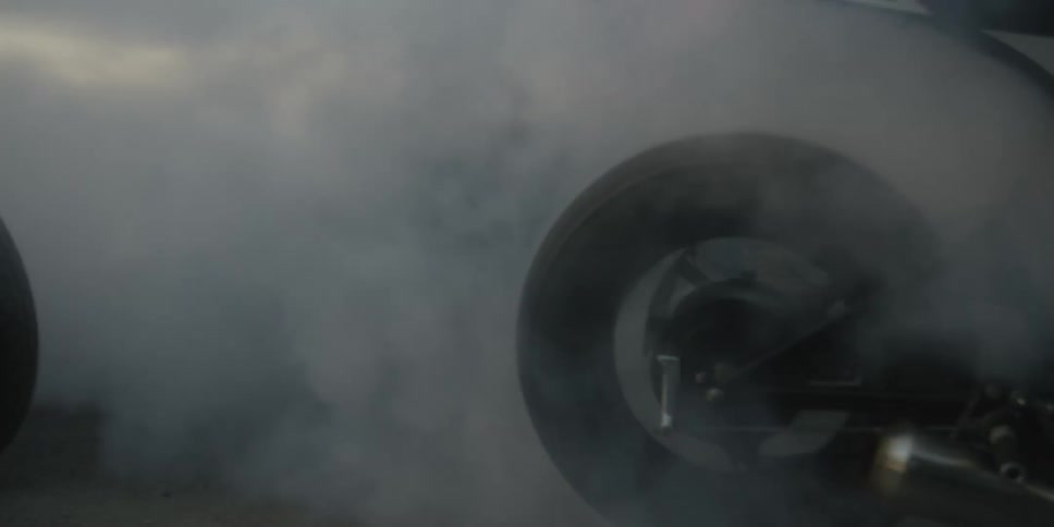 Several motorcycle riders spin their back wheels quickly creating clouds of smoke in the surroundings at night