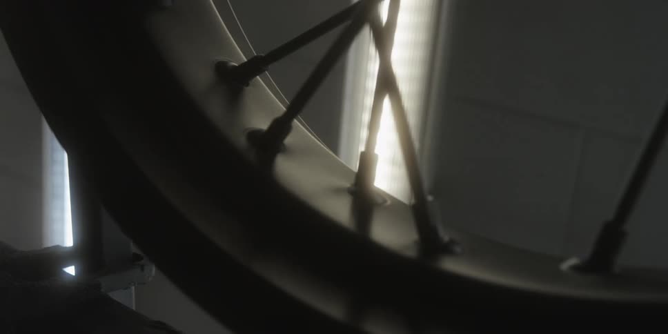 Bicycle wheel in closeup showing a dark rim and spokes with light in the background