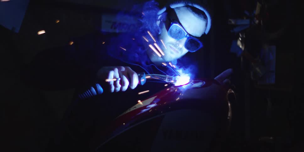 A man uses a welding torch while he is welding metal for a motorcycle