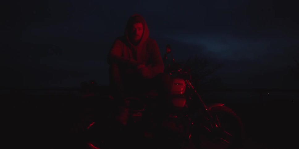 A man poses with his motorcycle while outside at nighttime