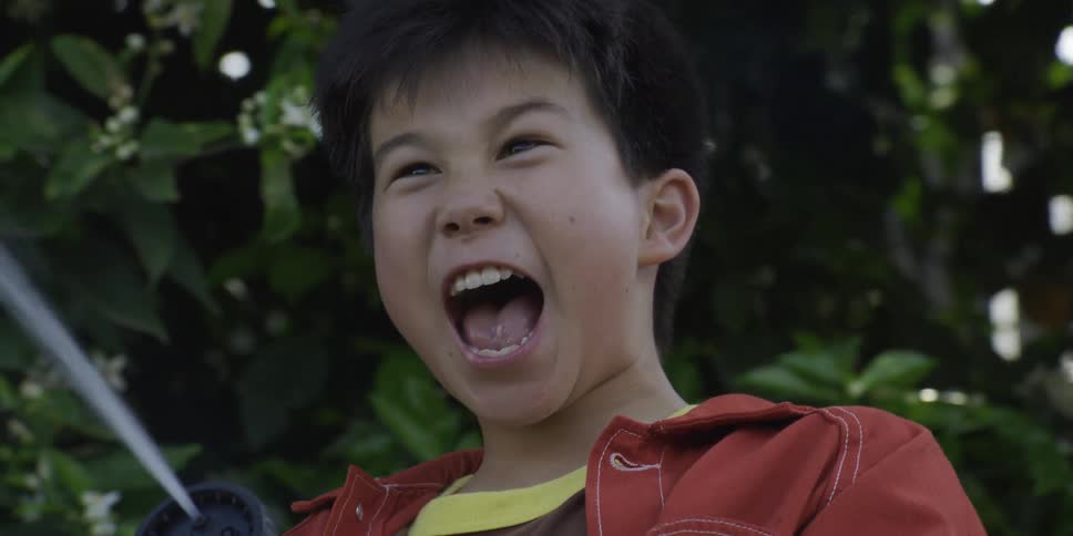 A young boy screams with delight while spraying water from a garden hose