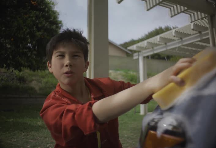 A boy washes a car with a soapy sponge outdoors on a sunny day