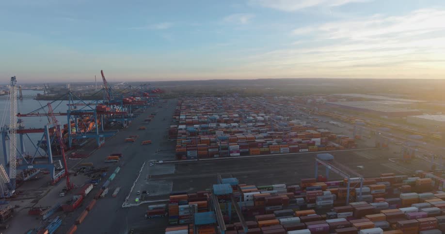 Shipping containers stacked on the loading dock with cranes along the coast of the shipping harbor