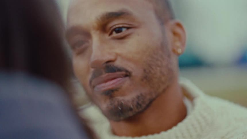A bearded man in a cream sweater gazes affectionately at a companion while listening intently