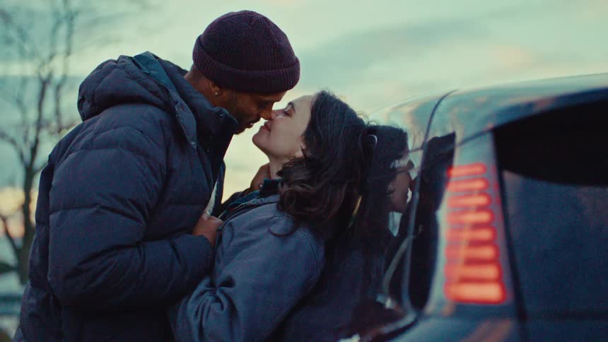 Couple leaning against a car sharing a kiss outdoors