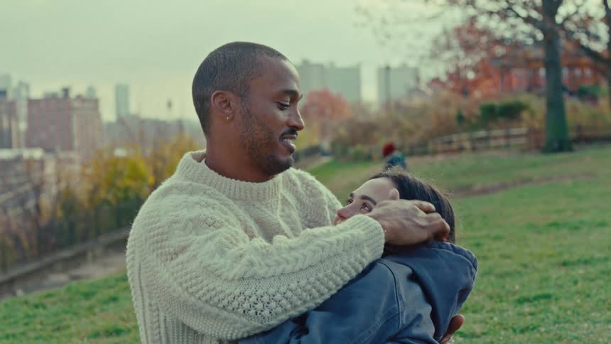 Couple sitting on a grassy area while the person on the left kisses the others forehead
