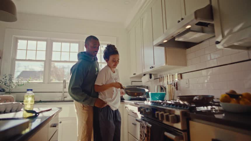 Couple in a kitchen while the person in front flips food in a frying pan on the stove