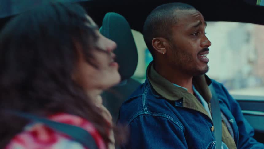 Young adult man driving a car and singing and laughing next to another young adult woman singing indoors during day time