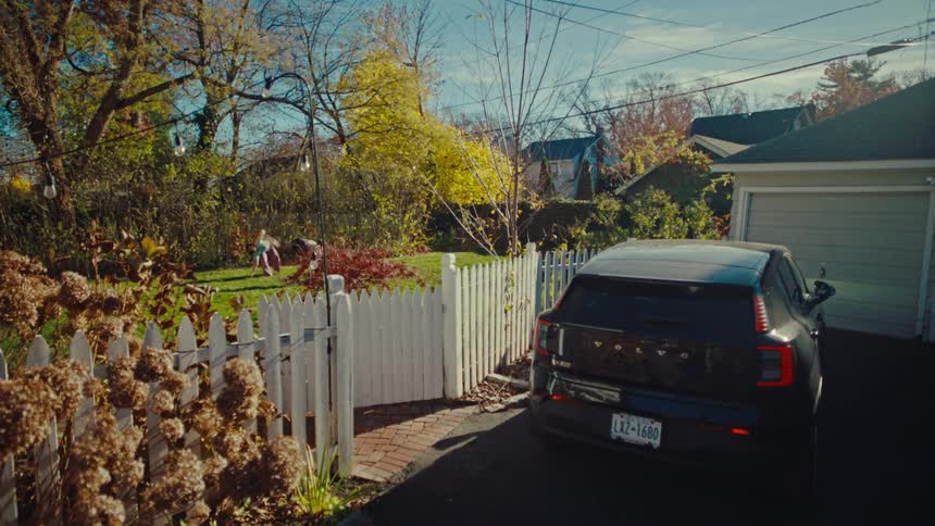 Backyard with a white fence and two people on the lawn in the background near a parked car