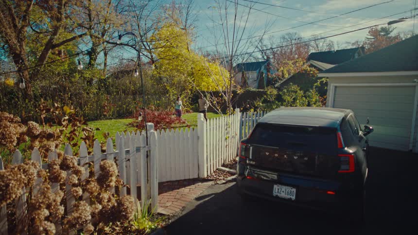 Automobile in the driveway of a neighborhood house as people play in the yard