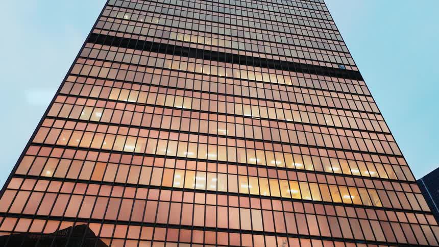 Modern skyscraper viewed from below highlights glass facade with interior lights under clear sky