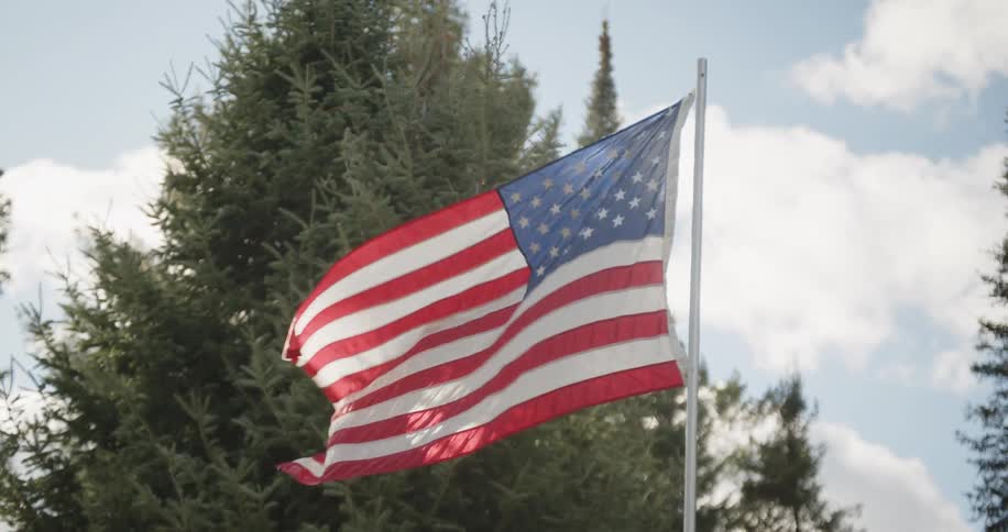 An american flag flaps in the wind on sunny but cloudy day